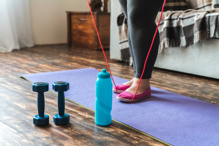 Woman at home standing on yoga mat legs close-up holding jump rope