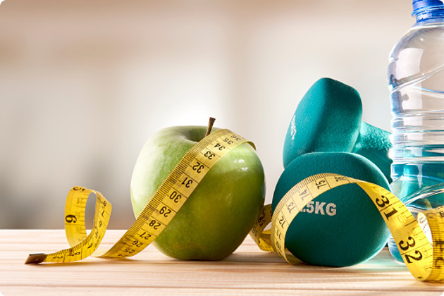 Dumbbells with apple, mineral water bottle and tape measure on wood