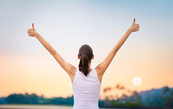 Women facing a sunset holding two thumbs up