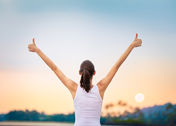Women facing a sunset holding two thumbs up