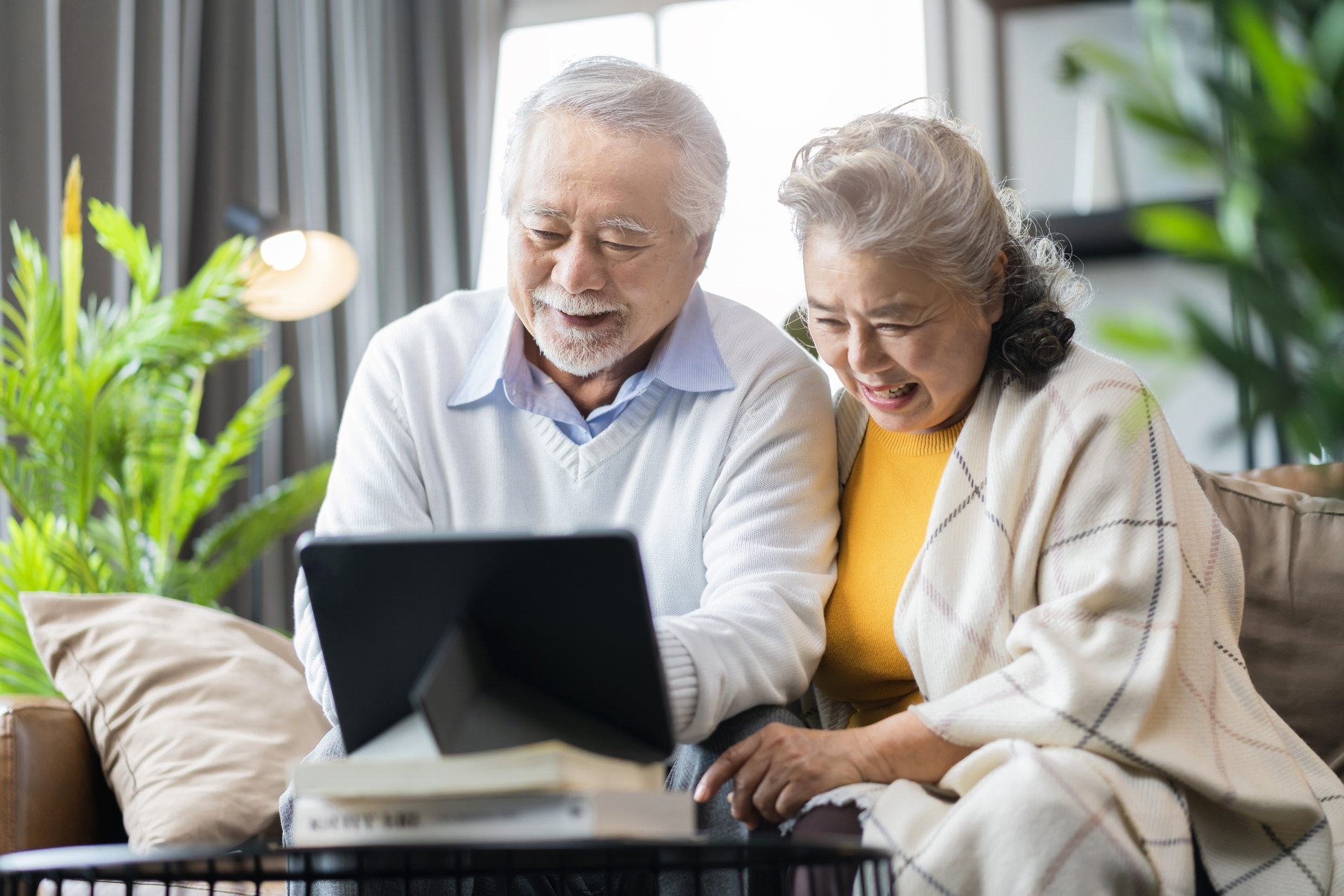 old asian senior couple retired age sitting on sofa couch video call to their family with tablet device social connect home isolation stay home state order concept,happiness senior laugh smile joyful