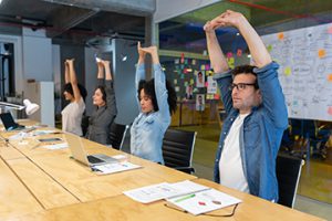 Group of workers at a shared desk doing an overhead stretch