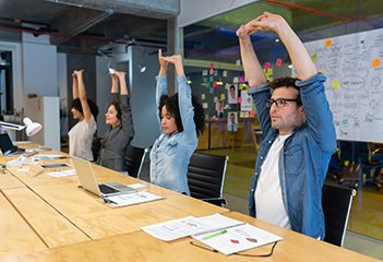 Group of workers at a shared desk doing an overhead stretch