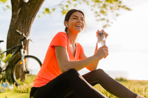 Smiling beautiful woman drinking water in bottle doing sports in morning in park