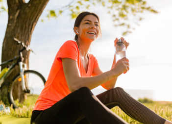 Smiling beautiful woman drinking water in bottle doing sports in morning in park